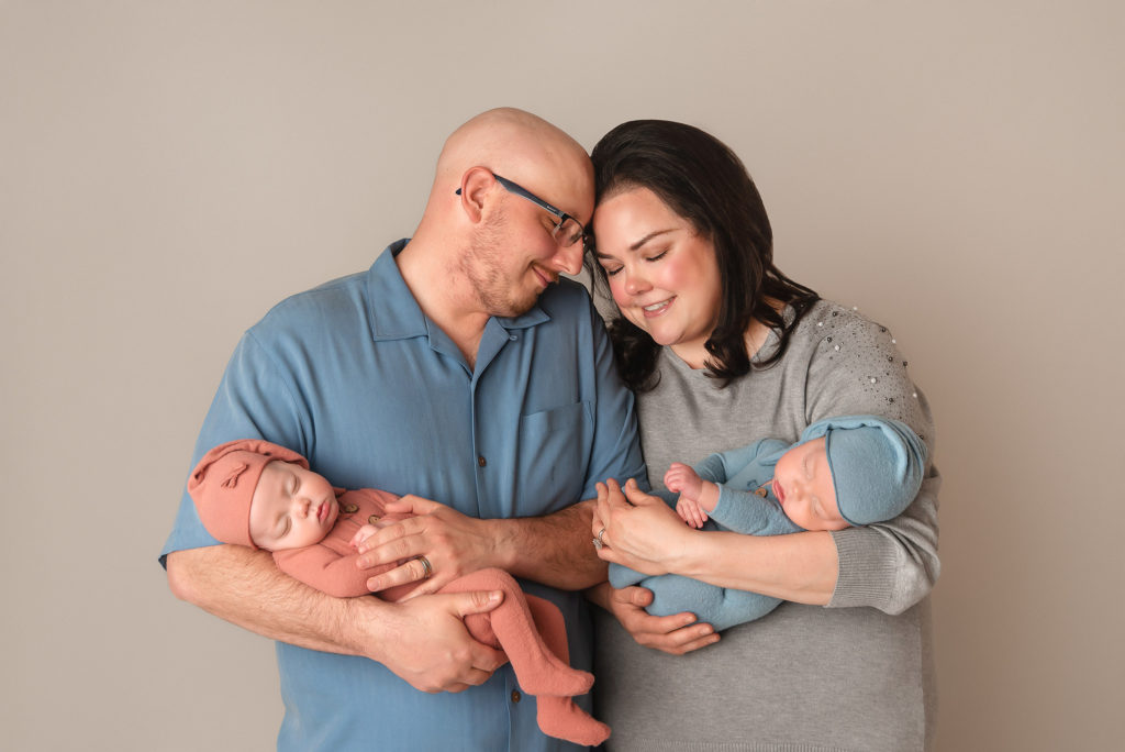 parents lean heads together holding new twins during newborn photos